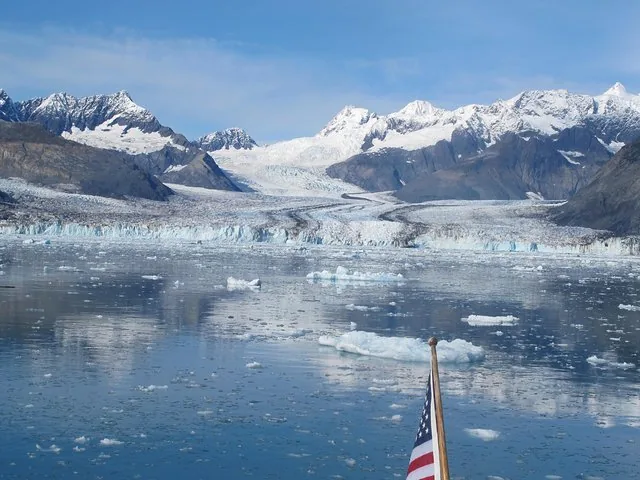 Scenic view of a glacier and snow-capped mountains across icy water.