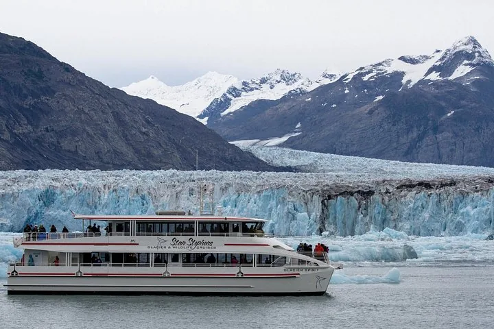 A Stan Stephens cruise boat passes a massive glacier and snowy peaks.
