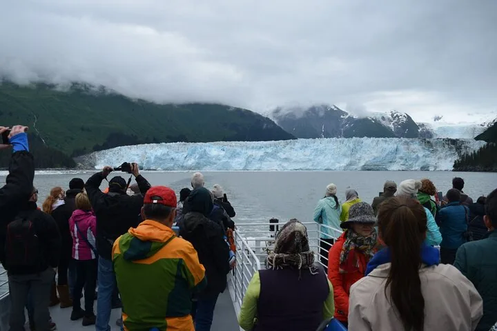 Tourists on a boat taking photos of a massive, wide glacier.