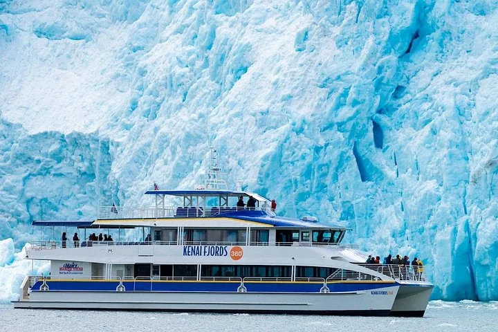 A Kenai Fjords tour boat positioned right in front of a towering blue glacier.